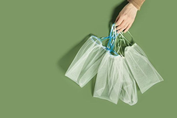 手握可重复使用的农产品袋，diy纺织品，水果和蔬菜可重复使用的包装，带领带的网袋，环保和零浪费的概念，平铺在橄榄色的背景上图片下载