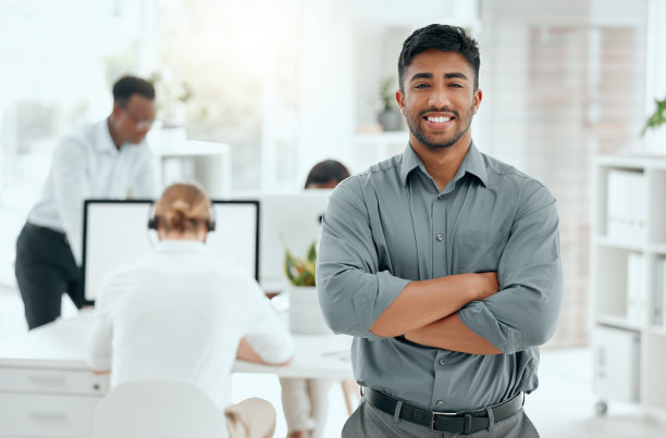 裁剪过的一个英俊的年轻商人的肖像，双臂交叉站在办公室里图片下载