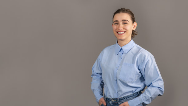 年轻的女商人，双手插在口袋里，面带微笑，对着镜头摆姿势。她在摄影棚拍摄时穿得很随意。图片下载