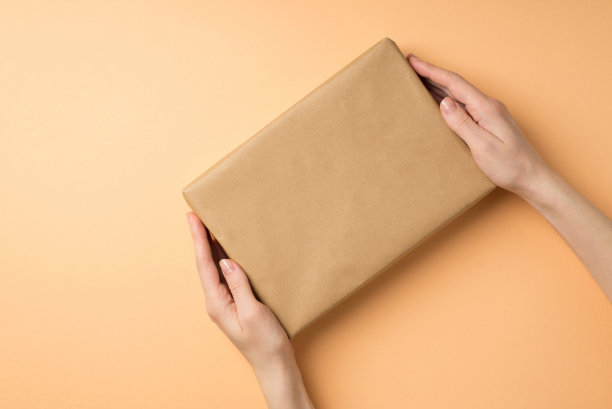 第一人称俯视图照片的女孩的手给予牛皮纸礼品盒在孤立的米色背景与copyspace图片下载