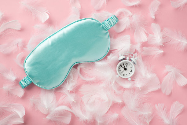 俯视图照片浅蓝色丝绸睡眠面具小白色闹钟和粉红色羽毛在孤立的粉彩粉红色背景与空白空间图片下载