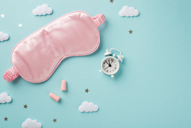 俯视图照片的漂亮丝绸粉红色眼罩小白色时钟与两个粉红色耳塞和一个五彩纸屑形状的小星星和云彩在孤立的空淡蓝色背景图片下载