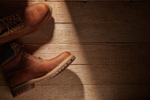 一双男子皮革棕色防水靴子在光线稀薄的阳光木制背景。鞋徒步旅行。男士时尚，鞋履新潮。平铺俯视图图片下载