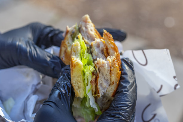 戴着黑色一次性手套的手拿着汉堡包。汉堡包已经吃了一半图片下载