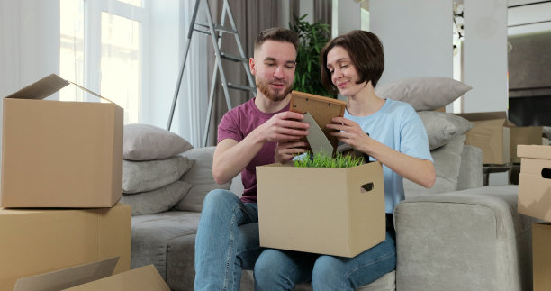 搬家那天，一家人坐在新公寓的沙发上，打开装着照片的纸盒。快乐的男人和女人搬进来，打开行李和家具。搬迁的概念。图片下载