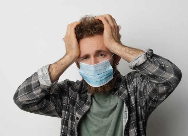 生病的年轻人戴着医用口罩，头偏头疼。帅哥觉得疼或者头疼。疲惫的年轻人试图集中精力按摩他的头部。卫生保健的概念。Covid 19概念图片下载