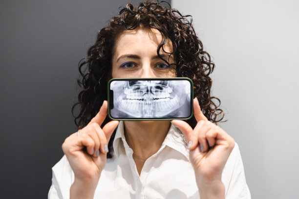 卷毛的女人在智能手机上展示下巴的全景照片。牙齿健康概念图片下载