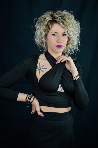 一个美丽的卷发金发女人的肖像，她用手调整她的黑色上衣图片下载