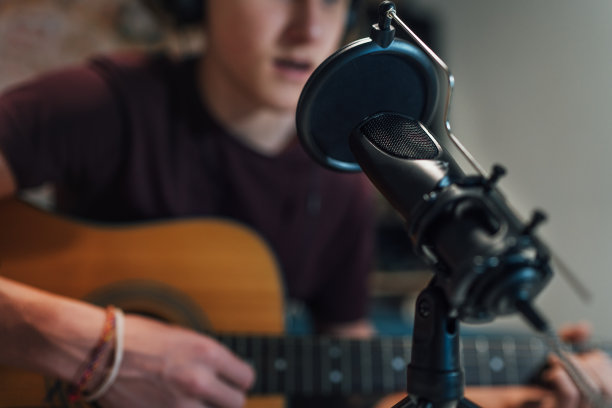 麦克风与流行滤镜特写照片与一个年轻的少年男孩在耳机录音和吉他演奏音乐。现代家庭录音室录音技术和青少年爱好理念。图片下载