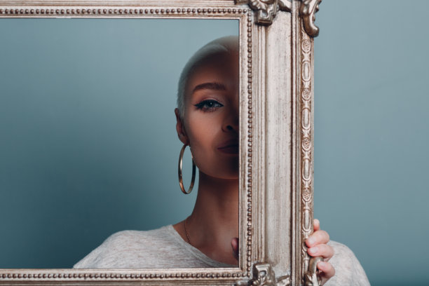 一名留着金色短发的千禧一代年轻女子，在她的头像后面，手里拿着一个镀金的相框。图片下载