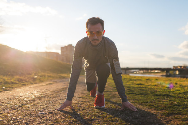 这是一个穿着运动服，戴着跑步太阳镜，准备冲刺的年轻男性跑步者的镜头图片下载