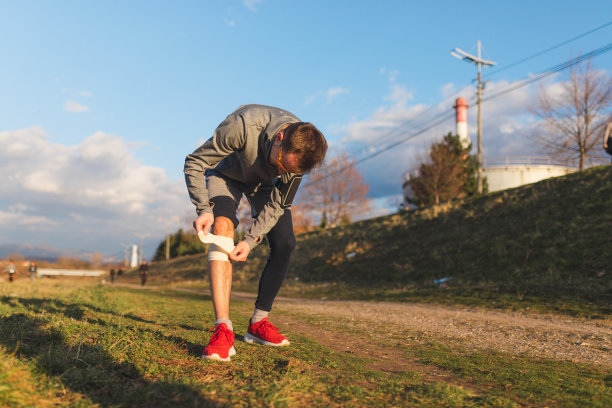 日落时，受伤的年轻男性跑步者在膝盖上缠着纱布图片下载