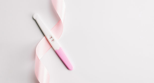 根验孕棒。孕妇试验阳性，白色背景上有粉色丝带。新的生活和新的家庭。母性、怀孕、节育概念。图片下载
