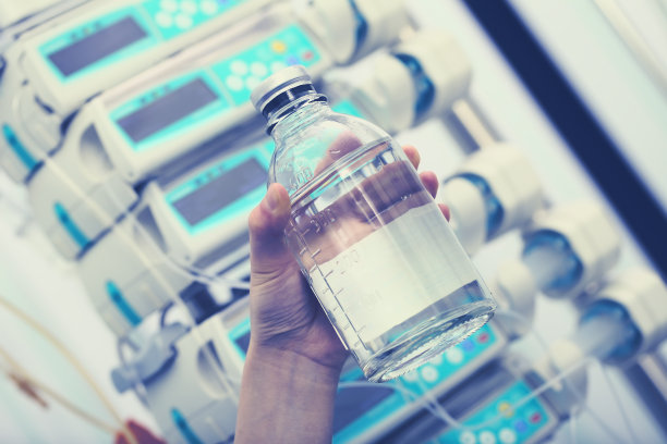 医护人员手持输液瓶，背景是医疗设备图片下载