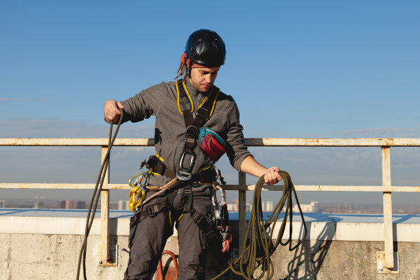一名穿着登山装备的白皮肤年轻工人在一幢建筑的屋顶上解开绳子图片下载