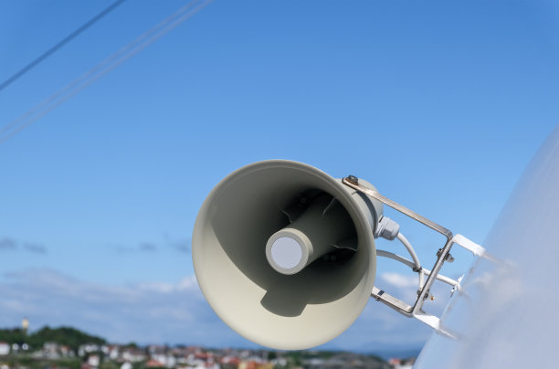 一个白色的火焰扩音器扬声器安装在户外，蓝色和部分多云的天空和景观在模糊的背景的特写图片下载