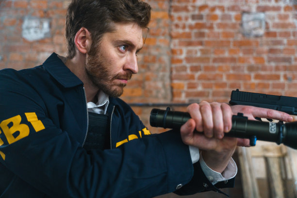 一个FBI探员的侧面肖像，拿着枪和手电筒，靠在砖墙上图片下载