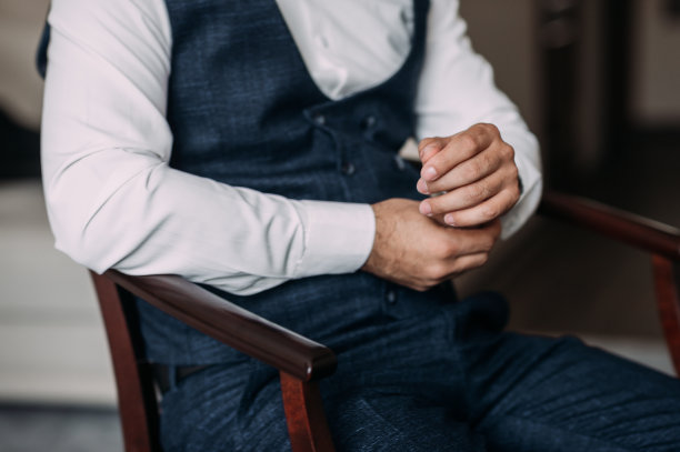 一个男人坐在木椅上紧张地摆弄着他的衬衫。图片下载