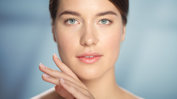 女性美丽的肖像。快乐的白人妇女与棕色的头发和浅绿色的眼睛摆姿势，触摸她的自然，健康的皮肤。柔软孤立背景下的健康护肤理念。关闭了。图片下载