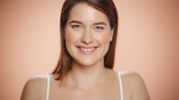 近距离的女性美丽肖像。快乐的高加索妇女与自然健康的皮肤，棕色的头发和浅绿色的眼睛摆姿势和微笑。柔软孤立背景下的健康护肤理念。图片下载