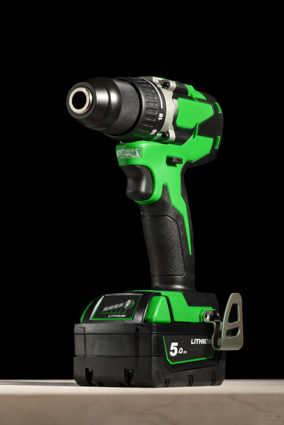 黑色背景的木桌上放着一把无绳螺丝刀。无绳钻，锂离子电池绿色。用于钻孔和驱动螺丝的专业工具图片下载