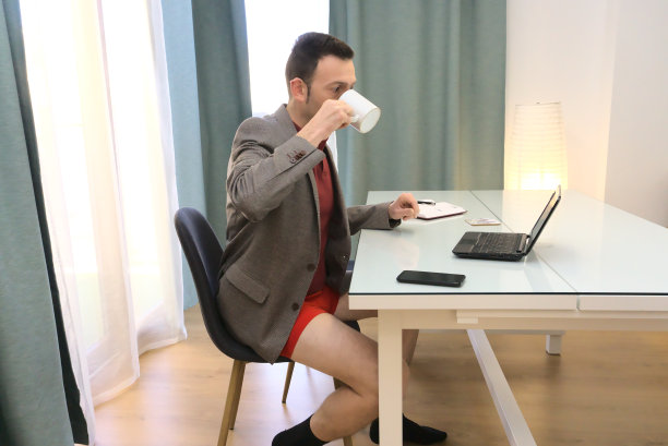 穿着西装外套和红色内衣的成熟男人在家工作，用马克杯喝咖啡图片下载