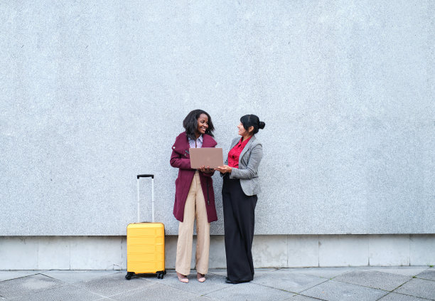 年轻的多种族女性穿着休闲服站在街上，在出差期间使用笔记本电脑图片下载