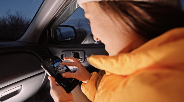 微笑的女人在车里用手机浏览婴儿照片。图片下载