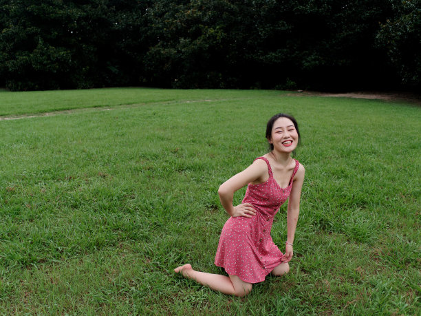 年轻的亚洲妇女跪在草地上赤脚在森林公园，美丽的中国女孩在性感的红色连衣裙享受她的无忧无虑的时间在阳光明媚的夏天，全长镜头。图片下载