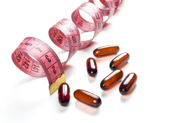 白色背景上的药丸和粉色卷尺。减肥概念、饮食、脂肪燃烧、健康饮食。图片下载