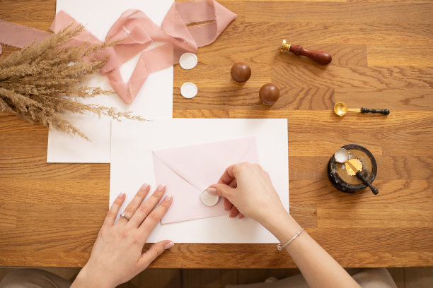 裁剪照片的妇女手制作问候信封工艺，装饰与粉红色的丝带和冲压。花在桌子上。图片下载