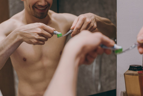 照片拍摄年轻微笑的半裸上身深色头发的男子，20岁，在镜子里刷牙在室内在浴室在家里人们保健每天早上例行的生活方式的概念图片下载