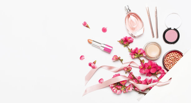 不同的妆化妆品。球腮红胭脂口红遮瑕瓶香水化妆刷春天粉红花在白色礼品包在灯光背景顶视图平躺。美丽时尚的背景图片下载