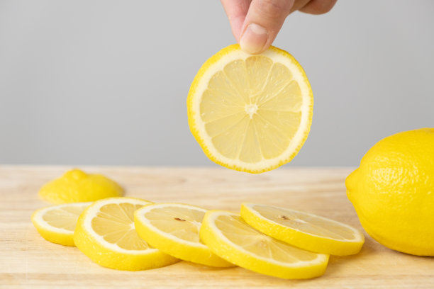 一位女士用指尖拿起一块放在木板上的柠檬片。图片下载