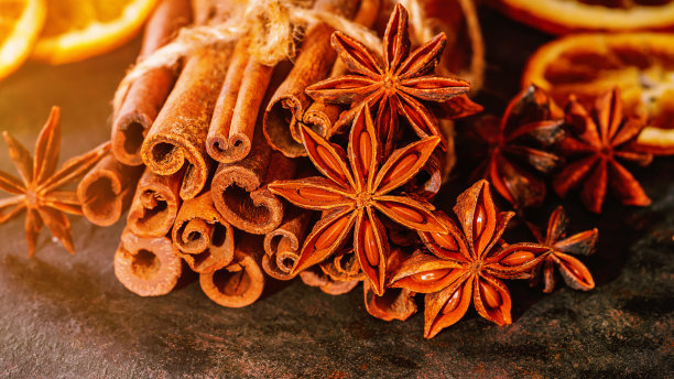 加香料的热葡萄酒。圣诞家居装饰。新年贺卡的背景。肉桂棒配八角茴香和橙子干，为秋冬暖饮做准备，背景为黑色。图片下载