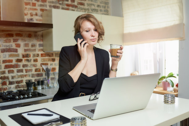 一个年轻的金发女人在家里的厨房里远程打电话。图片下载