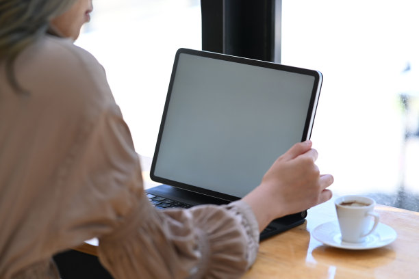 后视镜年轻女子坐在靠近玻璃的咖啡杯和使用电脑平板电脑。图片下载