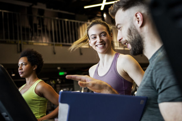 微笑的年轻女子和私人教练在健身房的跑步机上图片下载