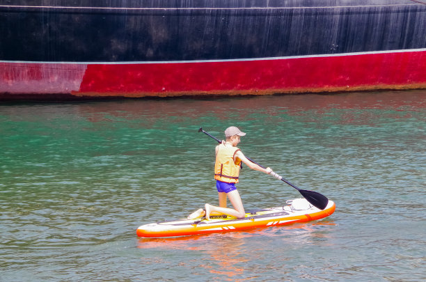 冲浪者在海里的一块板上游向一艘大船，侧视图图片下载