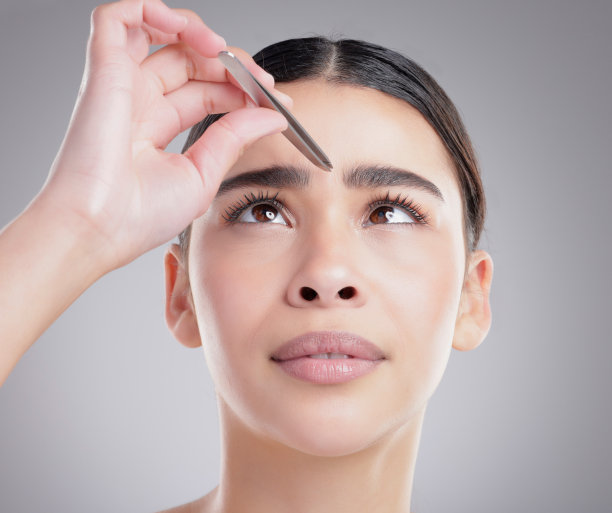一名迷人的年轻女子在灰色背景下拔眉毛的画室照片图片下载