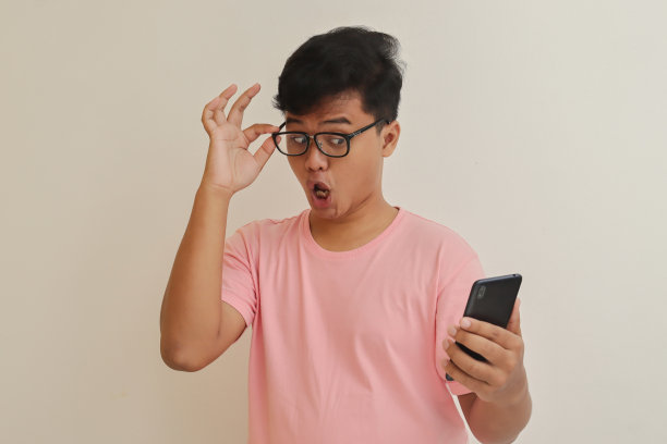 震惊的亚洲男子看着他的手机图片下载