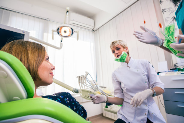 一个美丽的年轻女士坐在牙科椅上的特写，而stemmatologist(牙医)的手戴着无菌手套正在修复她的牙齿。图片下载