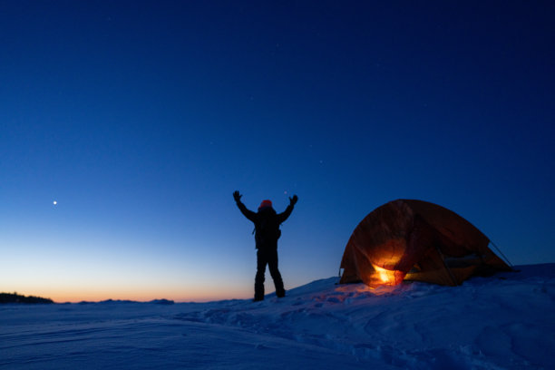 男子望向冰雪覆盖的雪地，背景是露营的帐篷图片下载