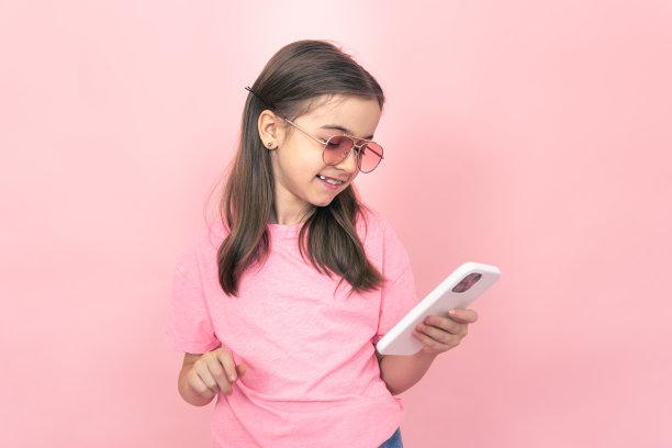 时尚的小女孩，粉红色背景的智能手机。图片下载