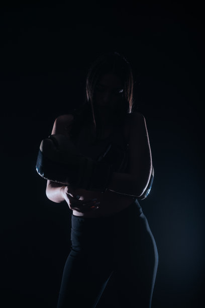 一个年轻的健身女孩戴上拳击手套的暗色对比的剪影肖像图片下载