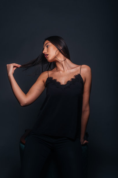 华丽的女模特与性感的黑色背心和黑色裤子摆姿势在一张椅子内的照相馆图片下载