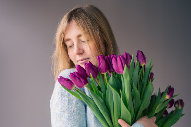 一个年轻女子的肖像与一束郁金香在灰色的背景。图片下载