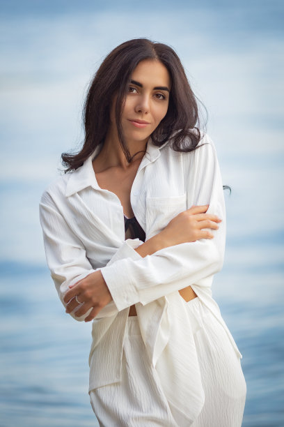 性感的年轻黑发女子在一个黑色比基尼和白色的西装摆姿势在海滩上图片下载