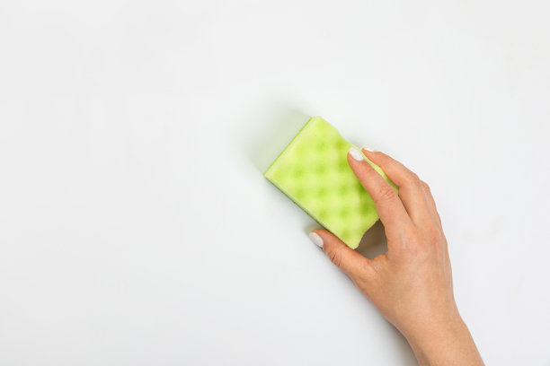 家庭主妇的手拿着一块海绵在灰色的背景上擦清洁剂。用于厨房、浴室和其他房间的各种表面的清洁剂。图片下载