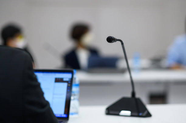 在讨论、会议、演示或会议期间，政治家或商人穿着西装，用笔记本电脑坐在麦克风前的木桌前。图片下载